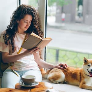 woman reading a book with her dog by a window